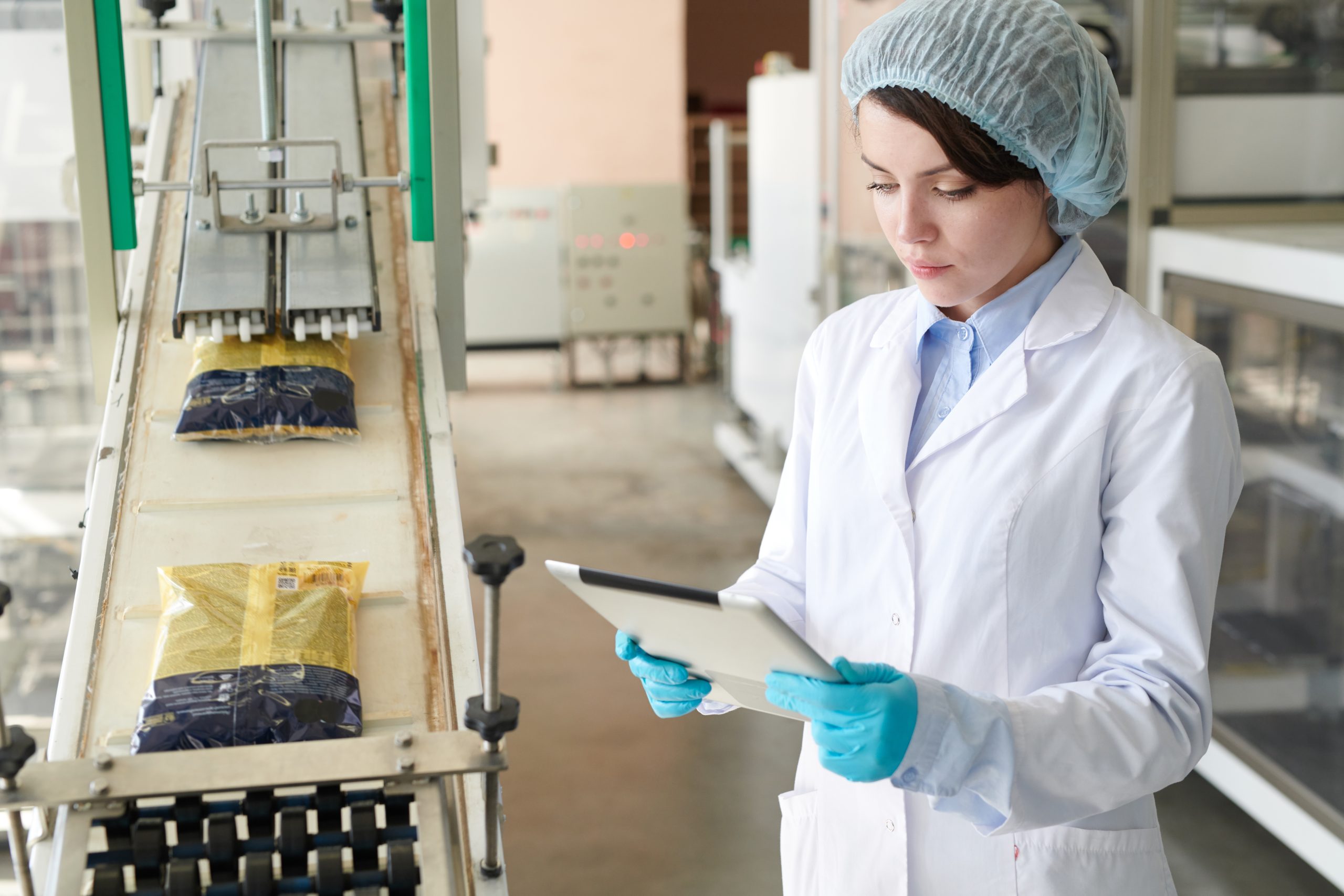 Waist up portrait of young woman controlling production  process at modern food factory and using digital tablet while standing by packaging line, copy space